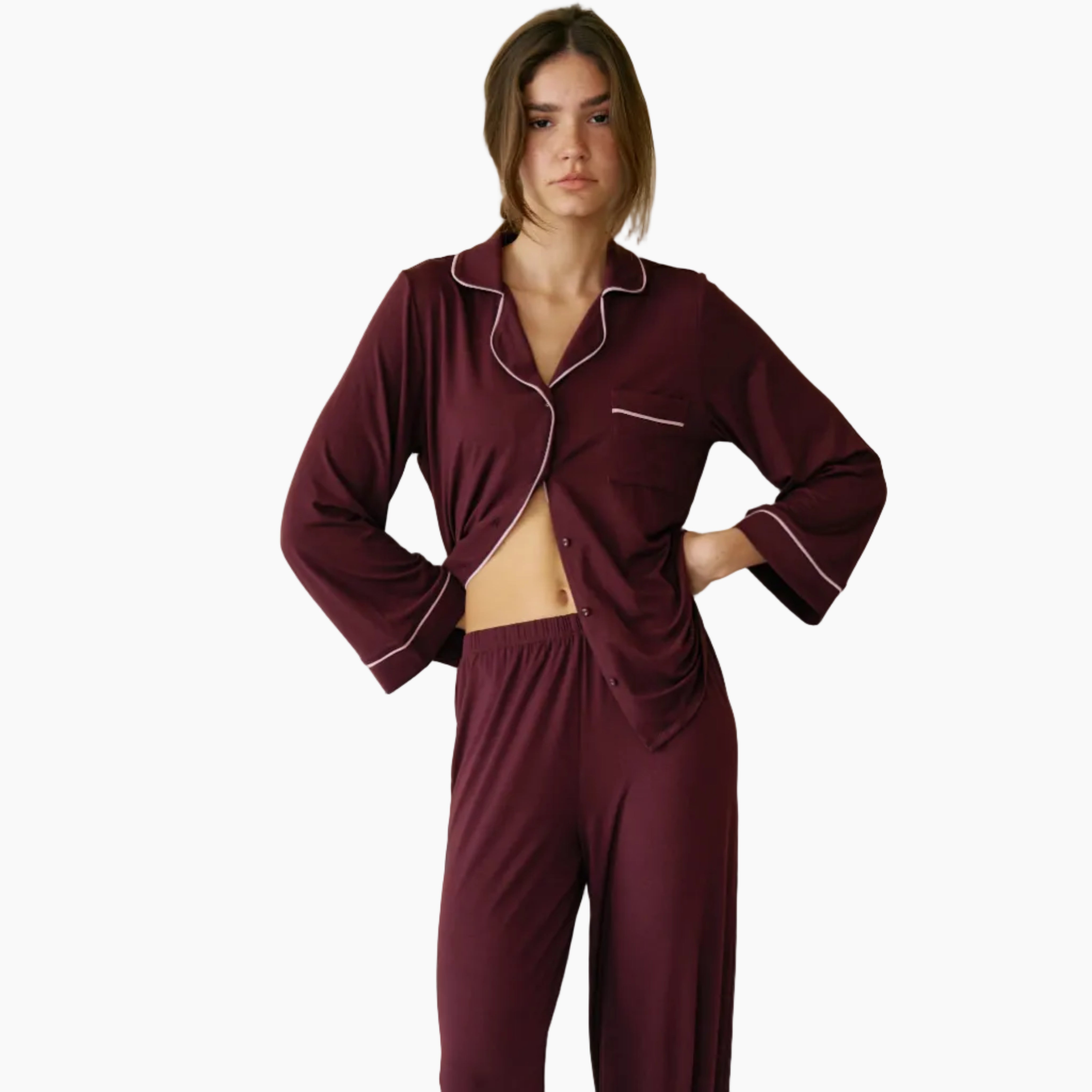 Person wearing burgundy pajamas with white piping on a white bed and background