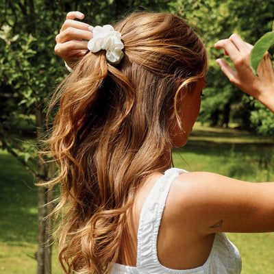 Silk Works Ivory silk scrunchie styled in a half-up hairstyle, photographed in natural sunlight against a green garden backdrop.