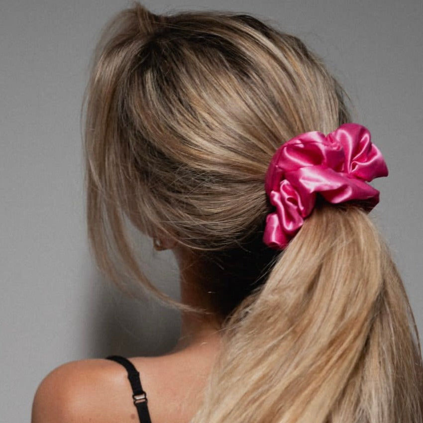 Close-up of a woman wearing a vibrant fuchsia pink silk scrunchie in her hair, highlighting the smooth texture and shine of 100% mulberry silk.