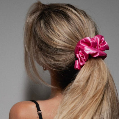 Close-up of a woman wearing a vibrant fuchsia pink silk scrunchie in her hair, highlighting the smooth texture and shine of 100% mulberry silk.