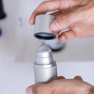 Male holding silver-coloured refillable deodorant with knurled texture. The lid is off and you can see the roll-on.