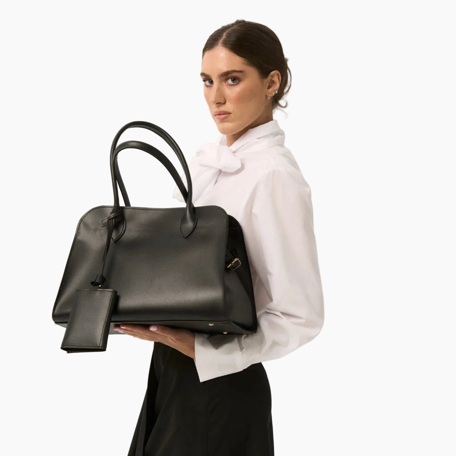 Woman holding a black handbag against a plain background