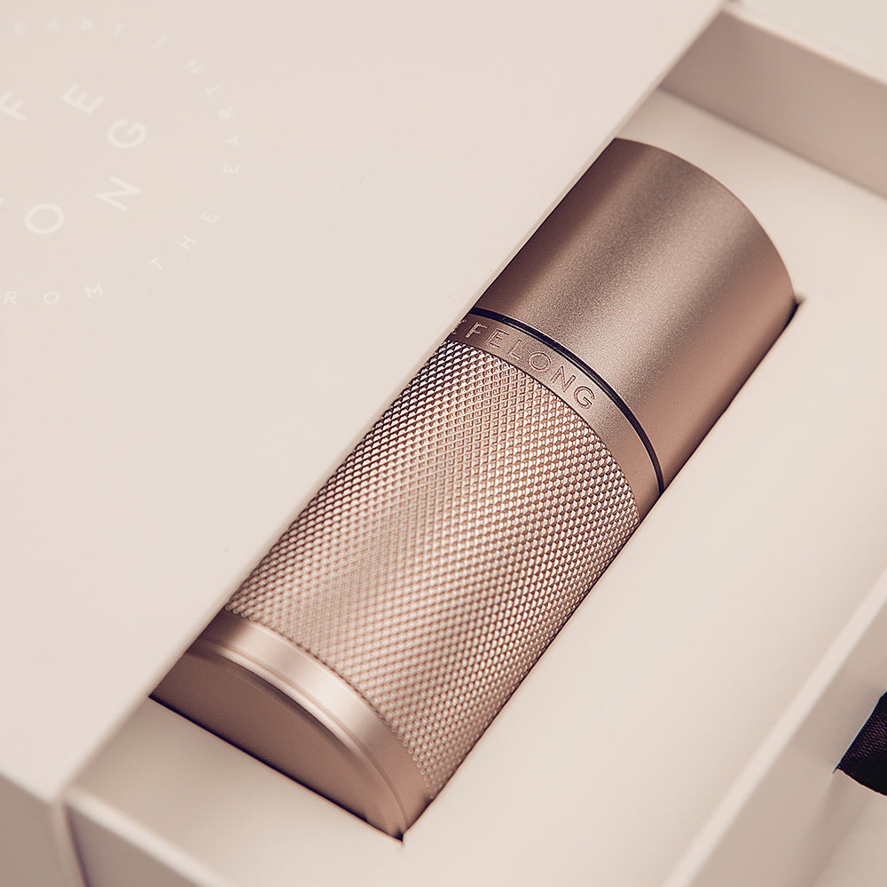 Rose-coloured refillable deodorant in a paper backage. The deodorant has knurled details and a black ring around it in the middle. The logo is place in the middle, saying LIFELONG