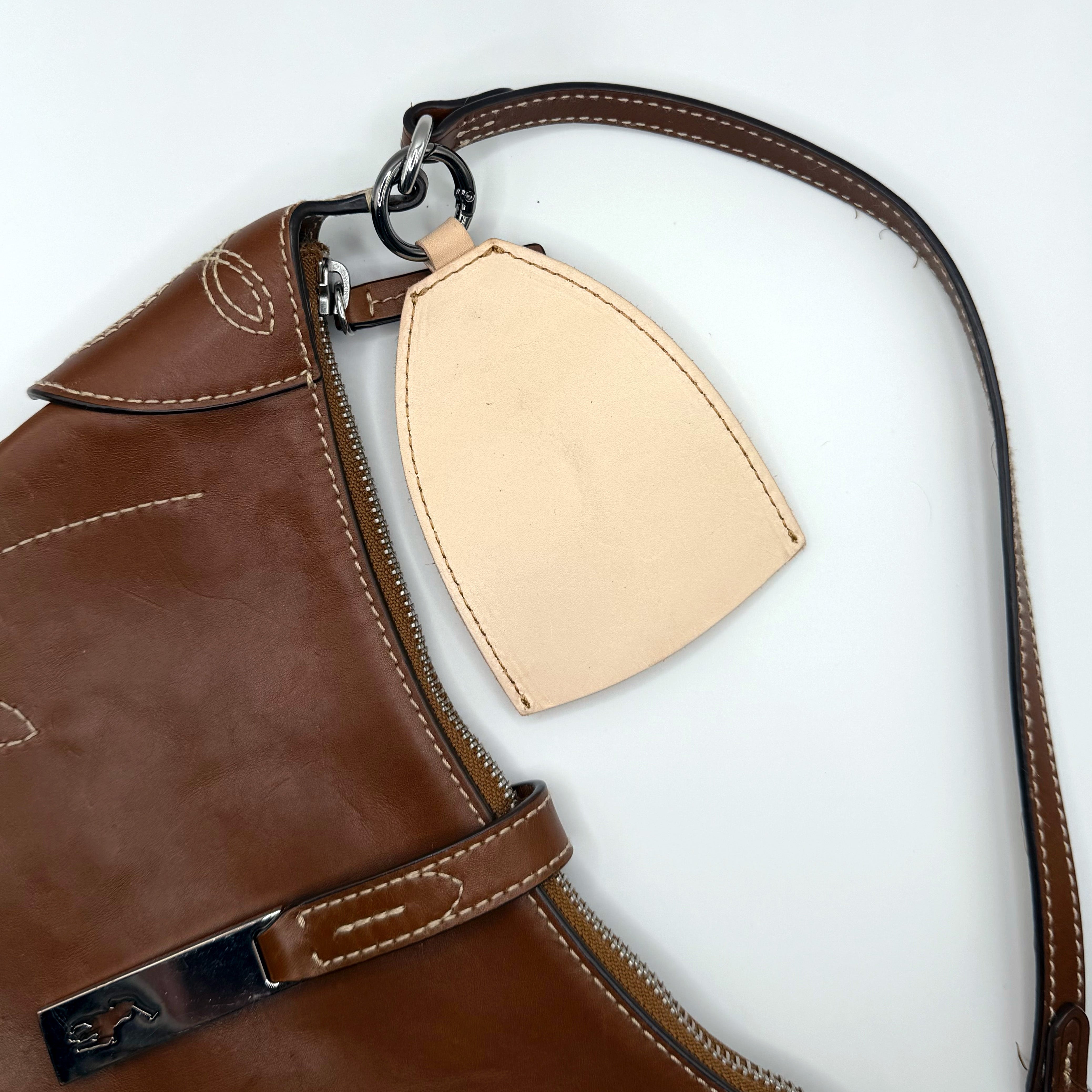 Brown leather bag with a beige leather tag on a white background