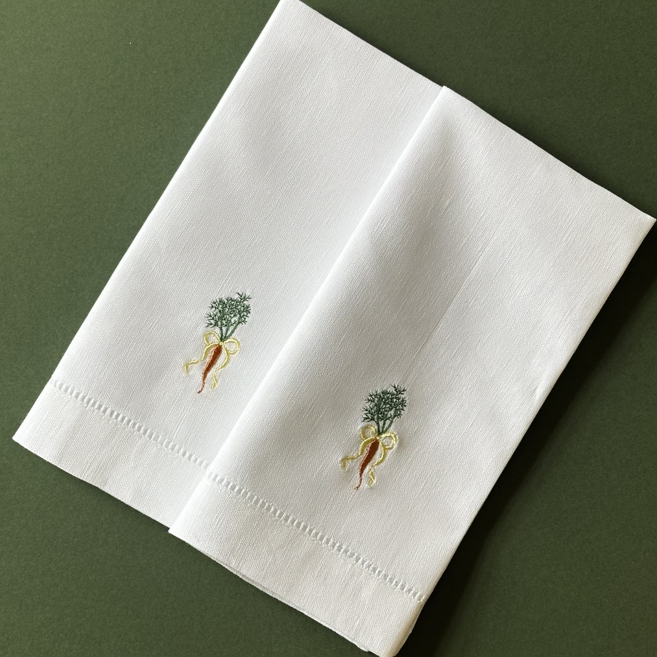 White napkin with embroidered carrot design on a green background