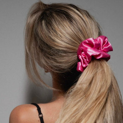 Lady wearing a large bright pink scrunchie in her caramel coloured hair.