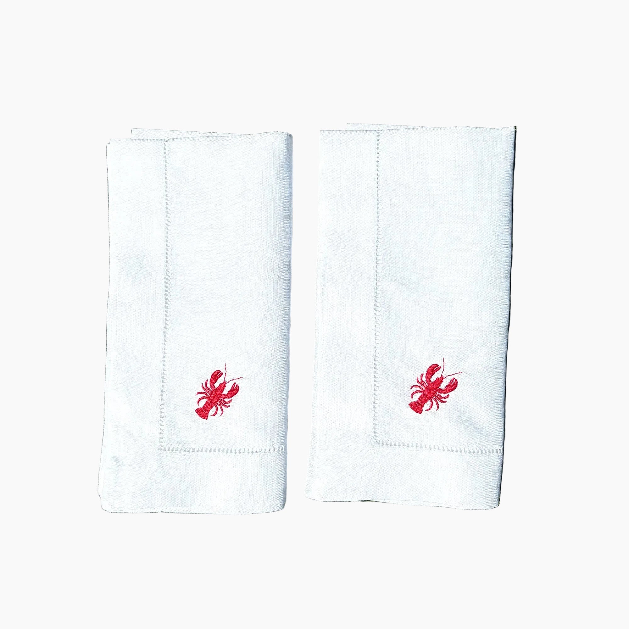 Two white napkins with red lobster embroidery on a grassy background
