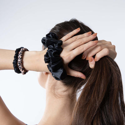 Woman holding her ponytail while wearing Silk Works mulberry silk scrunchies in black and leopard print, designed for gentle, frizz-free styling.