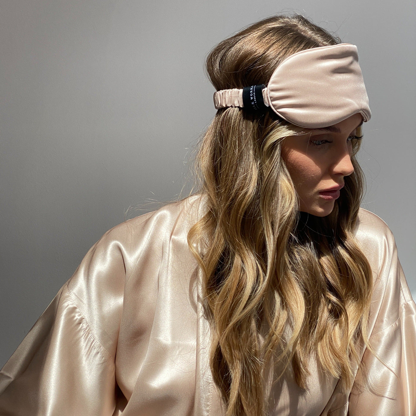 Model wearing a Silk Works caramel mulberry silk eye mask with matching silk robe, shown in soft natural light.