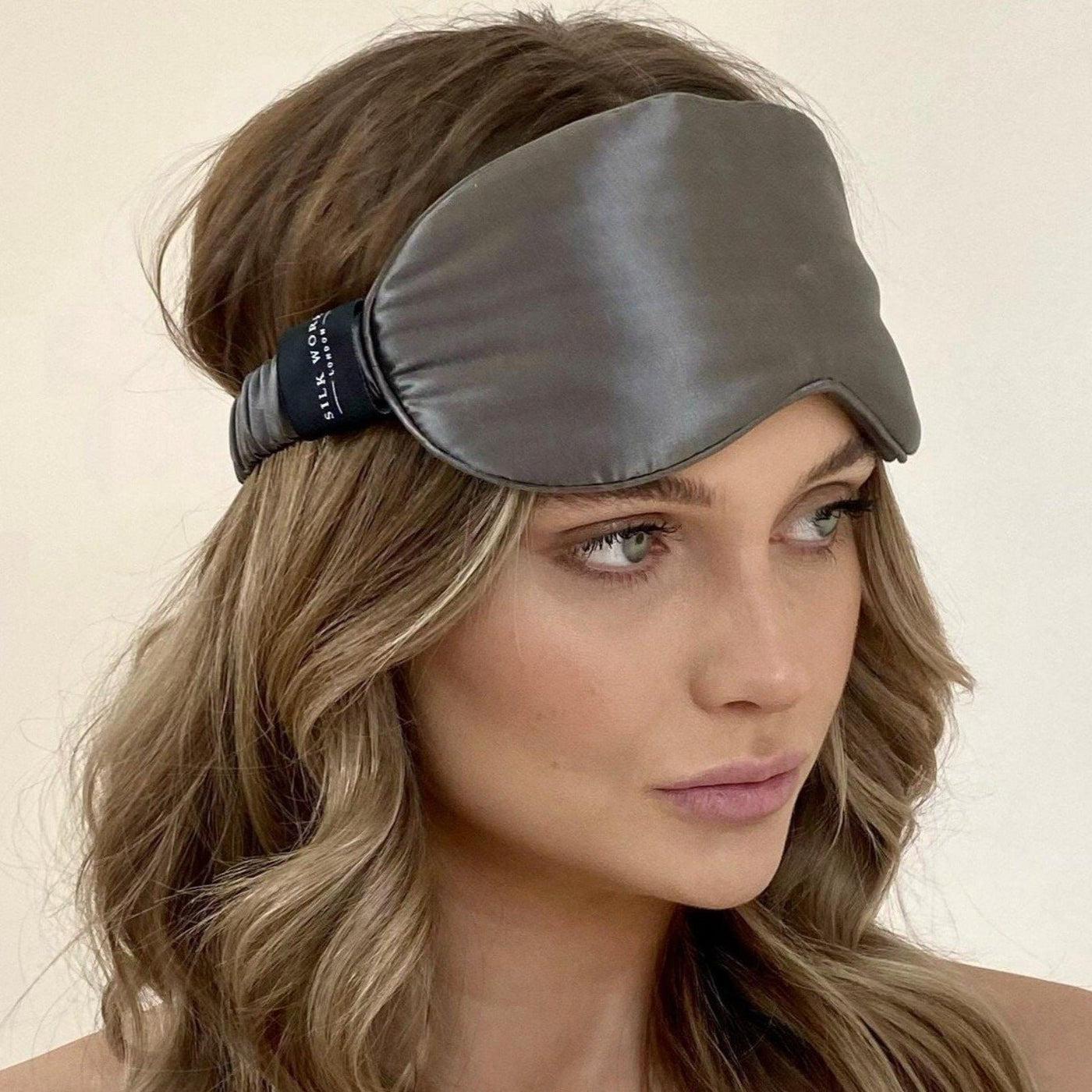 Model wearing a Silk Works charcoal grey mulberry silk eye mask with a soft ruched strap, styled with loose waves and a natural makeup look