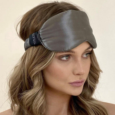 Model wearing a Silk Works charcoal grey mulberry silk eye mask with a soft ruched strap, styled with loose waves and a natural makeup look