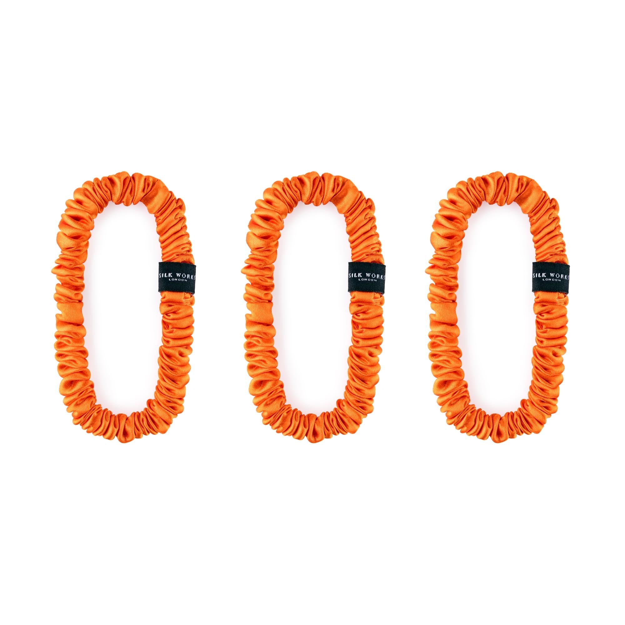 Trio of orange 100% mulberry silk skinny scrunchies by Silk Works, designed to reduce breakage and frizz.