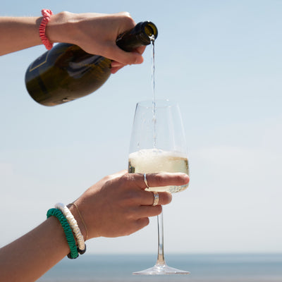 A hand pouring champagne into a glass, adorned with three elegant mulberry silk scrunchies on the wrist—effortless luxury in motion.