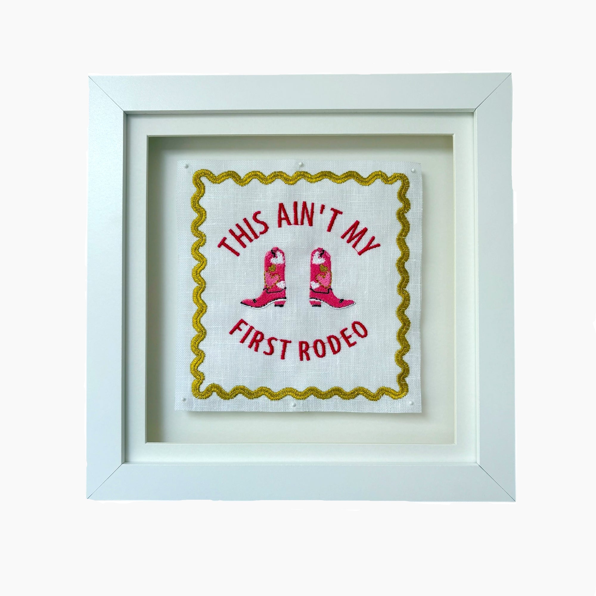 Framed embroidered artwork with pink boots and text on a white background