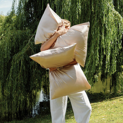 Silk Works caramel silk pillowcases styled outdoors in the sunlight held by a woman stood by a lake 